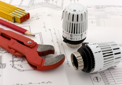 "Two thermostats for a new heating are combined with a ruler, a pencil and a pipe wrench on a blueprint."